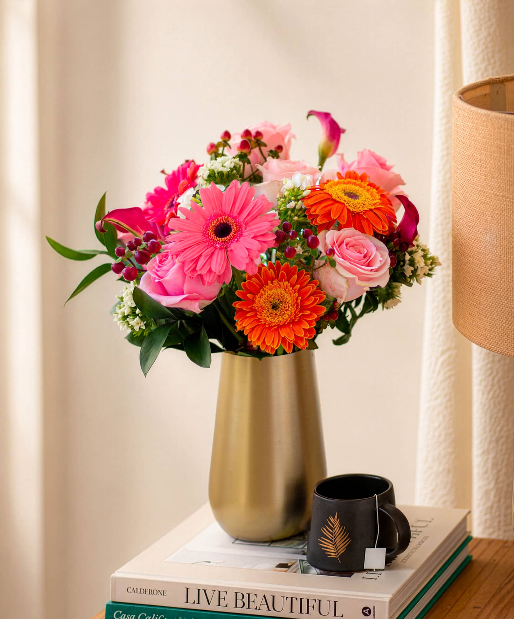 Vibrant floral arrangement with pink gerbera daisies, roses, and orange blooms in a vase.